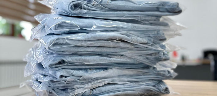 Pila de prendas dobladas, cada una empacada en bolsa de plástico transparente