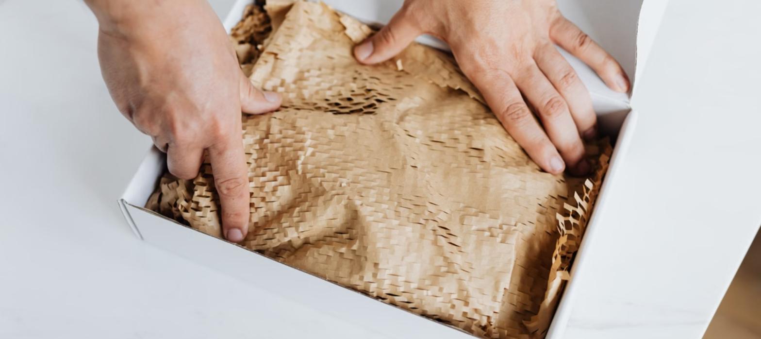 Manos colocando relleno de papel kraft en una caja de empaque sostenible